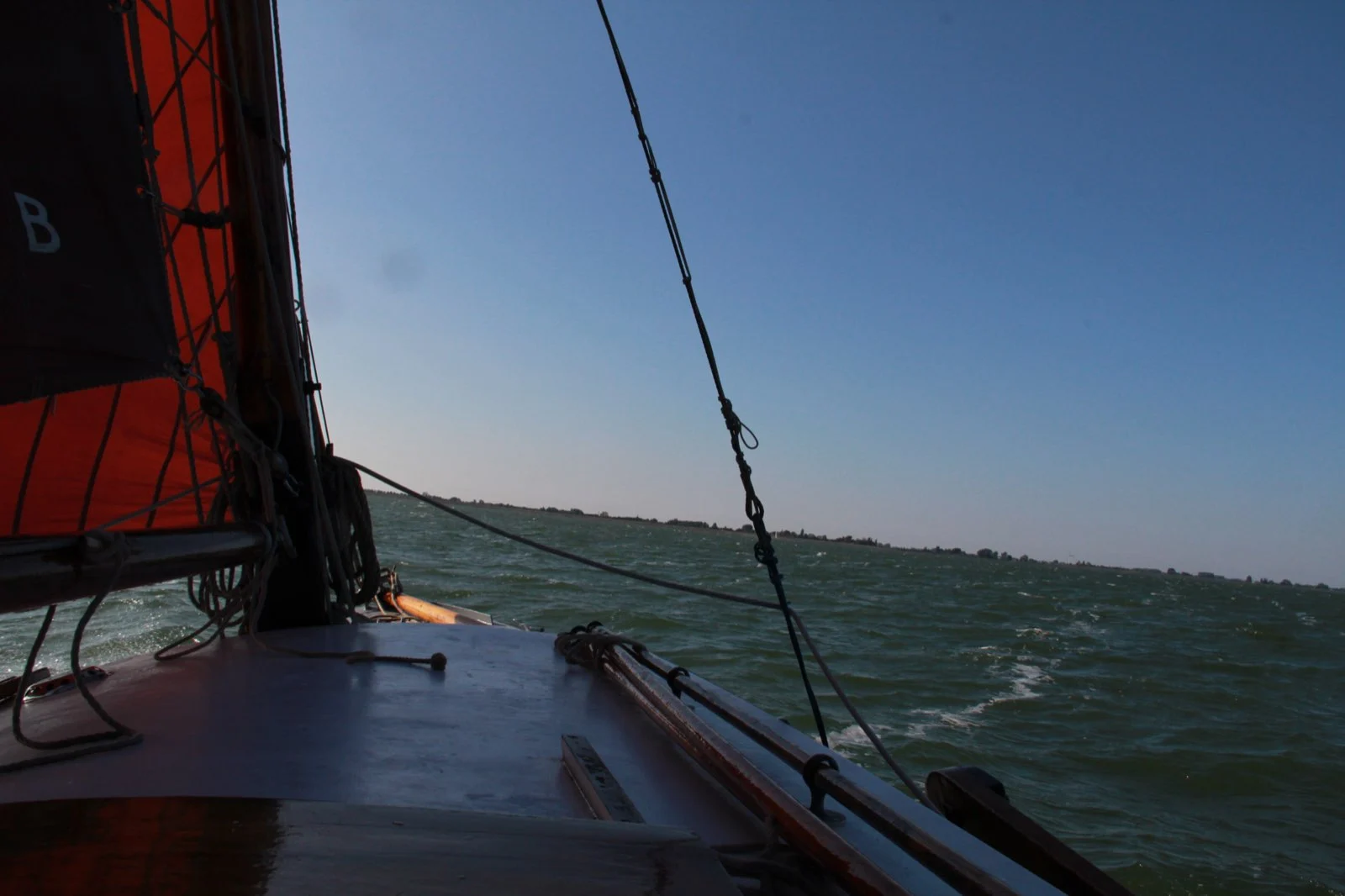 Zicht vanaf een platbodem met rood zeil op de Schelde